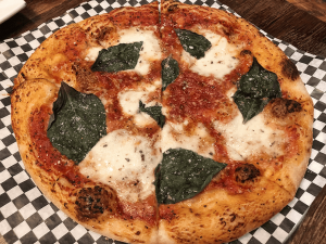 The margherita pizza presents fresh mozzarella, basil, and tomato sauce.