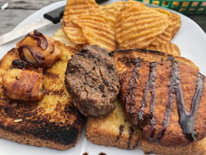 The Trifecta: One bacon-wrapped scallop, one crab cake, and one 3 oz. filet medallion all served open-faced on Texas toast, plus a side of homemade chips.
